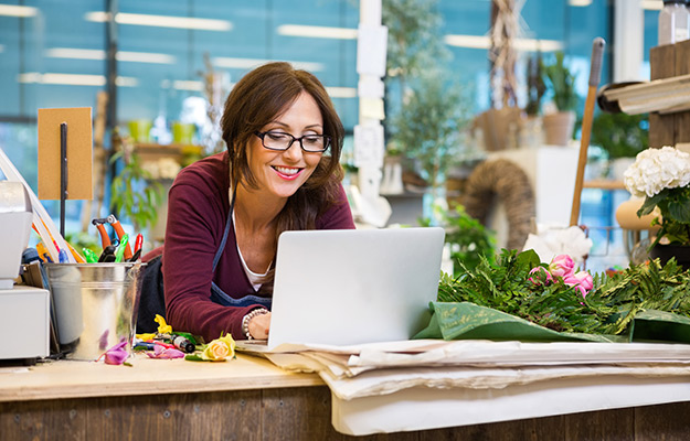 A flower store owner looking at the computer smiling | How Photos Can Increase Your Google My Business Listing Performance