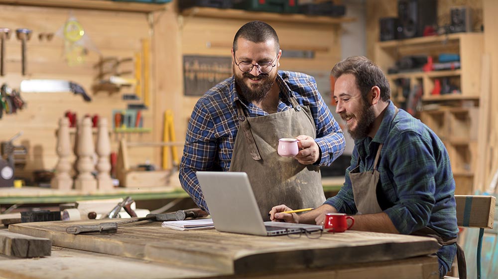 Two carpenters in a wood shop looking at a laptop